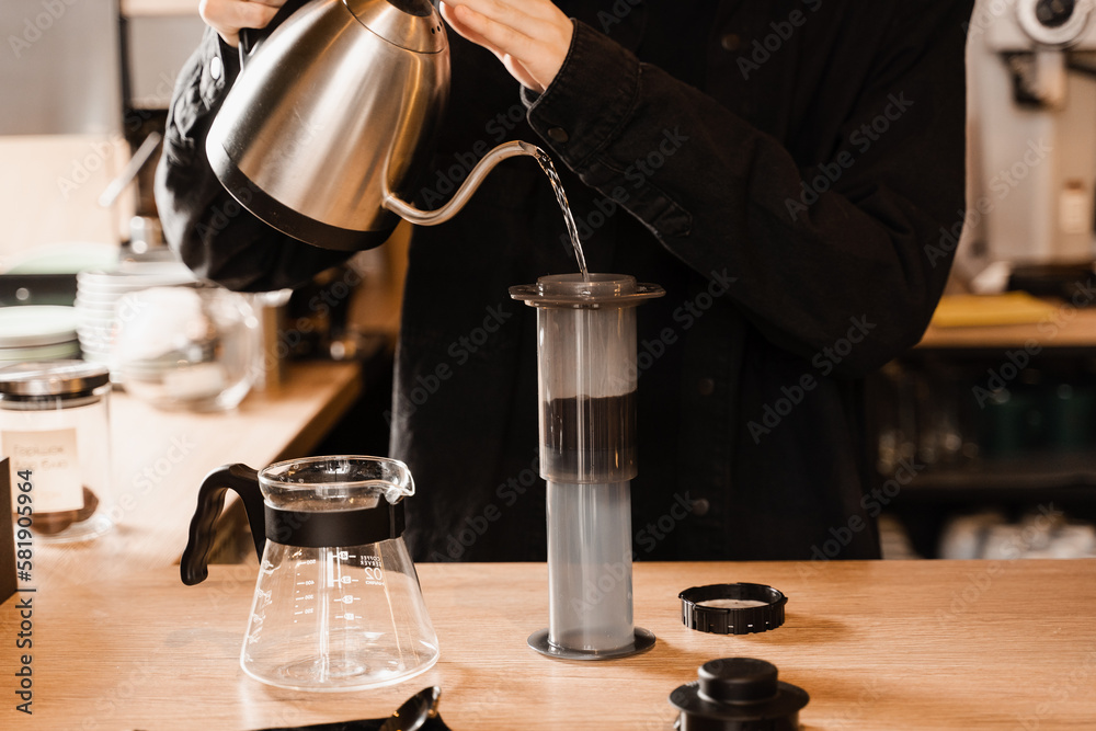 Pouring hot water over roasted and ground coffee beans in aeropress. Process of aeropress alternative method brewing coffee. Barista is brewing aeropress coffee in cafe.