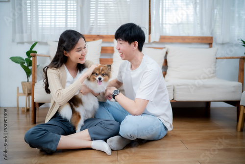 Couple of love looking each other while embrass their dog in girl's hug in front of couch, happy family concept. © Wanwajee