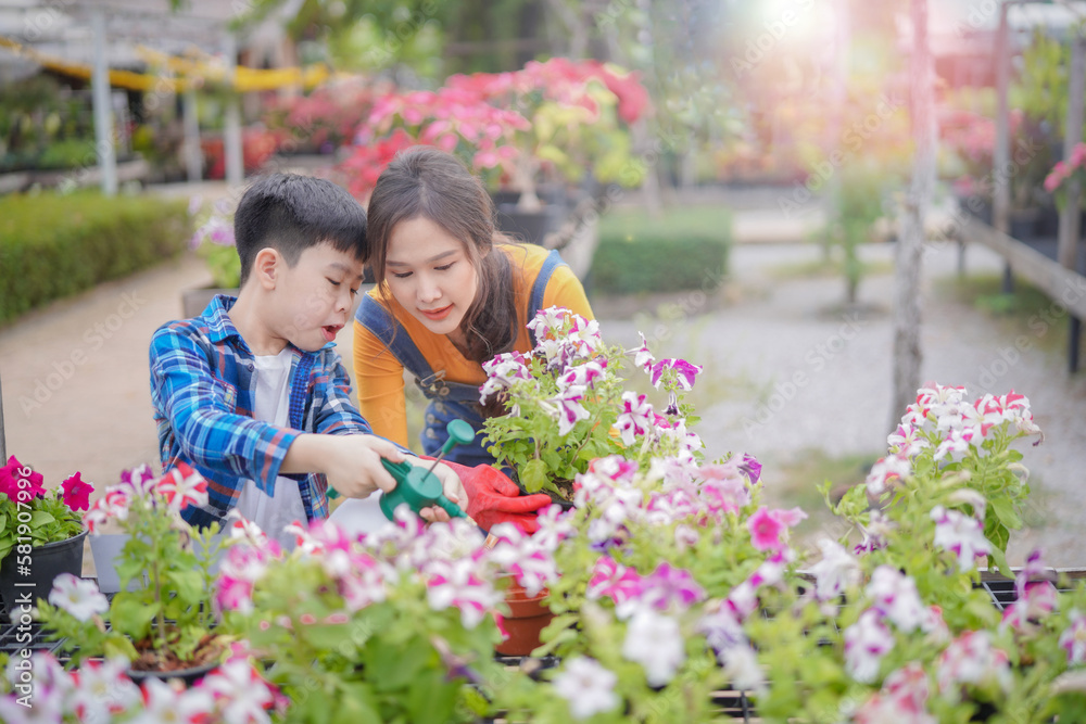 Son helping his mom sray nutrition to flower in their farm intensingly, kid boy and lady farmer.