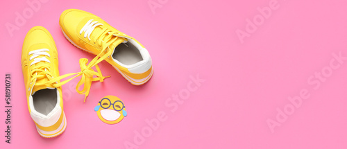 Sneakers with tied shoe laces and paper smile on pink background with space for text. April Fools' Day celebration