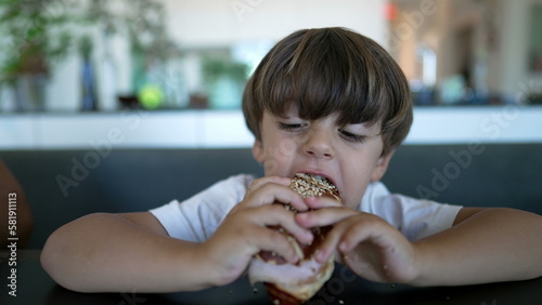 One little boy grabbing bread taking a bite of carb food seated at table