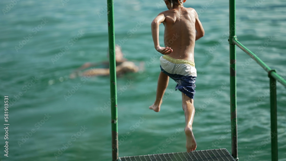 Fototapeta premium Kid plunging into lake water. Child having fun running by dock and jumps in river in super slow motion