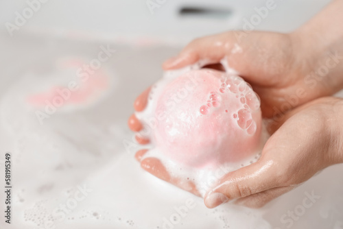 Woman with pink bath bomb above water, closeup