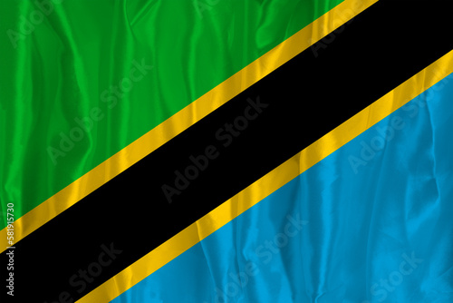 The flag of Tanzania on a silk background is a great national symbol. Texture of fabrics The official state symbol of the country