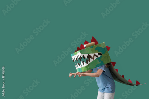 Fényképezés Little girl in cardboard dinosaur costume on green background
