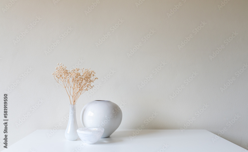 Dried baby's breath flowers in white vase on table against beige wall (selective focus)