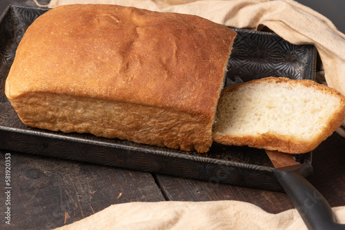 A golden brown, freshly baked loaf of artesian sourdough bread, sliced once in a vintage pan. photo