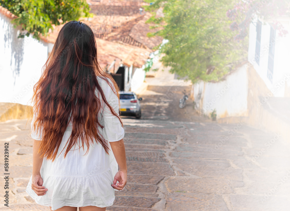 Naklejka premium beautiful woman from behind with a white dress and long hair in a town in Colombia