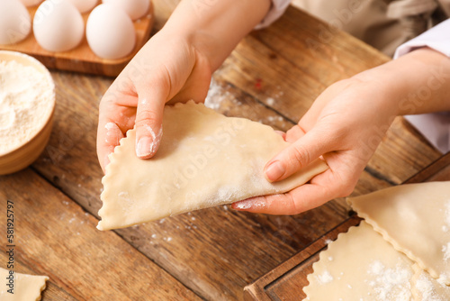 Female hands with raw meat empanadas on wooden background, closeup