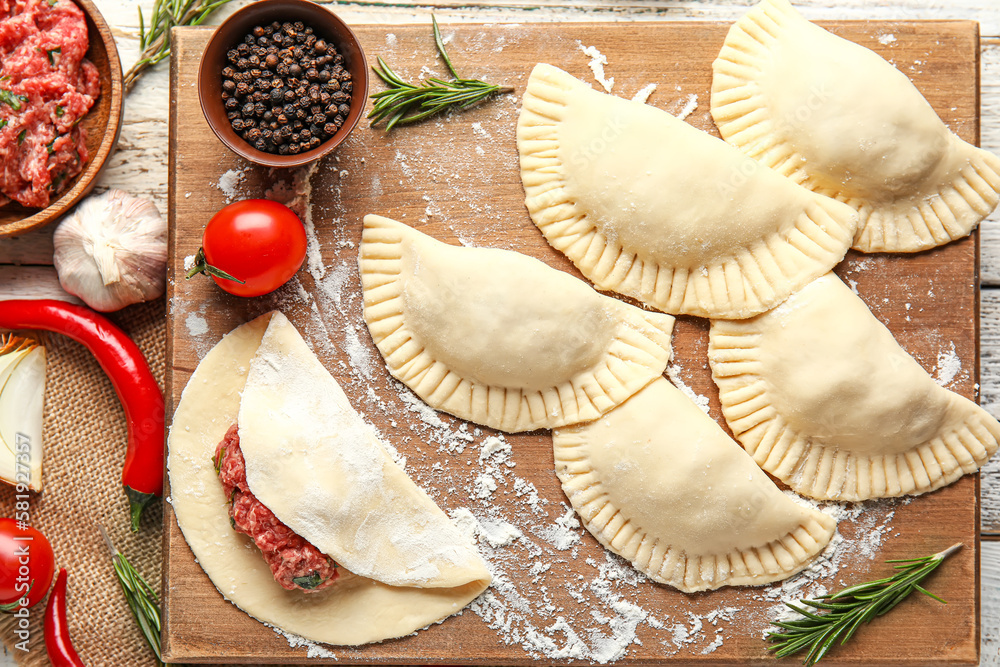 Board with raw meat empanadas and ingredients on light wooden background, closeup Board with raw meat empanadas and ingredients on light wooden background, closeup