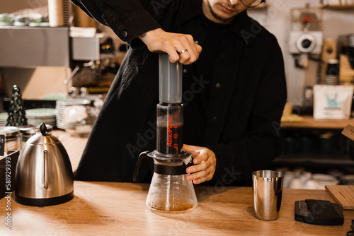 Aeropress coffee. Barista is pushing aeropress for pouring coffee drops trought aeropress to pot. Alternative scandinavian coffee brewing method.