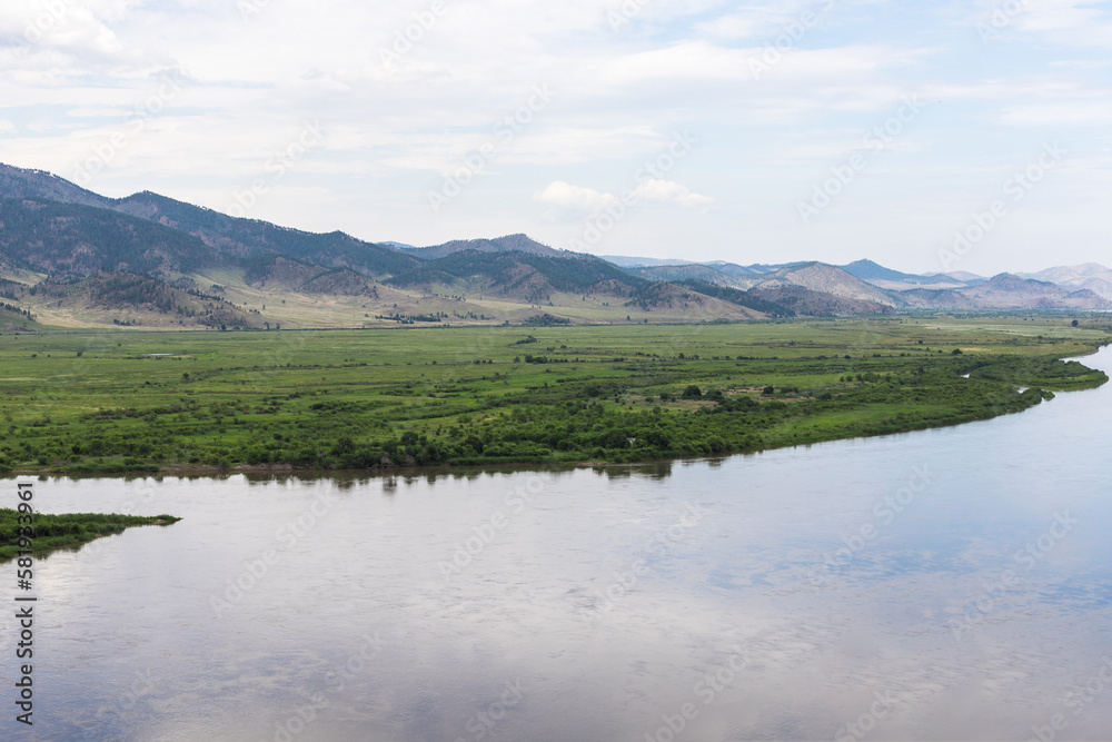 Landscape of a beautiful large Selenga river against the background of mountains, steppe and blue clear sky. The sky is reflected in the river. Beautiful summer landscape