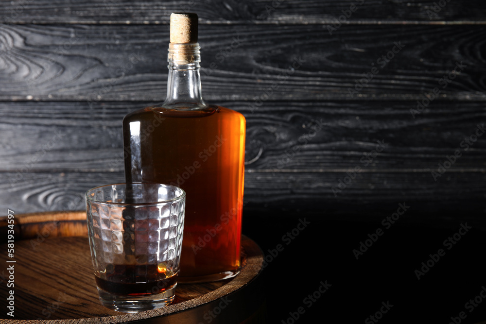 Glass and bottle of tasty whiskey on barrel against dark wooden background Glass and bottle of tasty whiskey on barrel against dark wooden background