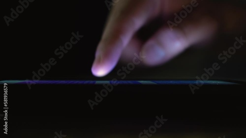 A person checking on his phone during the night. Bright touchscreen in the dark. Browsing social networks. Selective focus of a person using his phone.