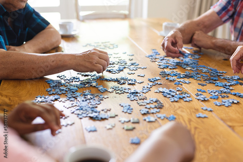 Hands of diverse senior friends sitting at table doing jigsaw puzzle together photo