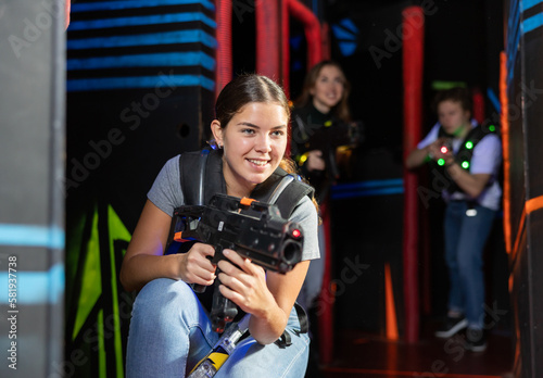 Positive girl holding laser pistol playing laser tag game with his friends