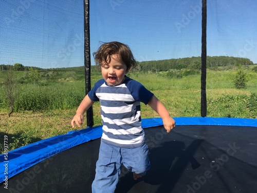 little curly cute child runs waving his arms and jumping on the trampoline with singing