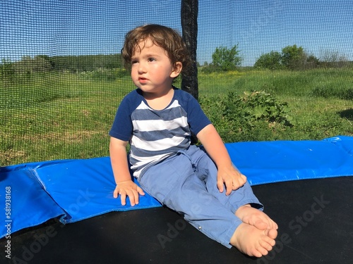 looking into the distance thoughtful cute curly boy sitting on a trampoline