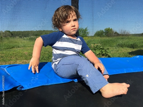 little boy cute child thinking.  pokes a finger at a trampoline and looks into the distance sits on a trampoline