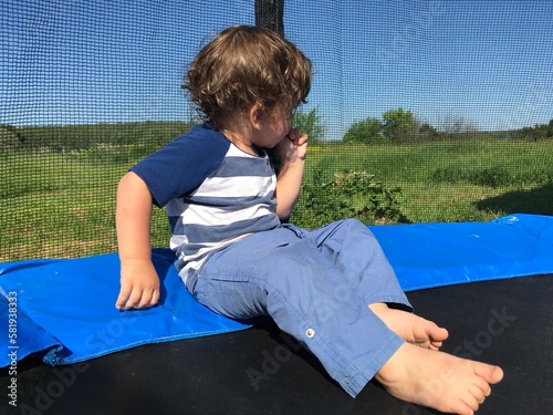 turning away looks at nature pensive cute curly child sits on a trampoline