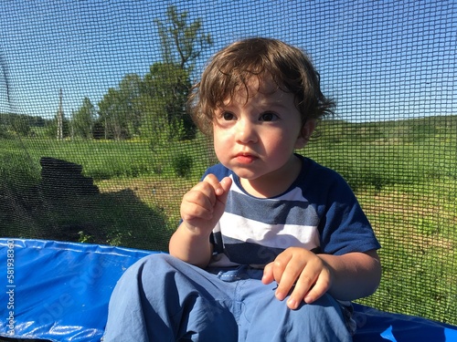 cute smiling child with big eyes sits resting on a trampoline looks attentive listens