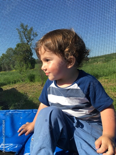 curly cute child sits resting on a trampoline looks with a gentle playful look