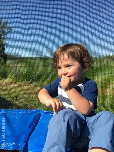 curly cute child sits resting on a trampoline looks with a gentle playful look