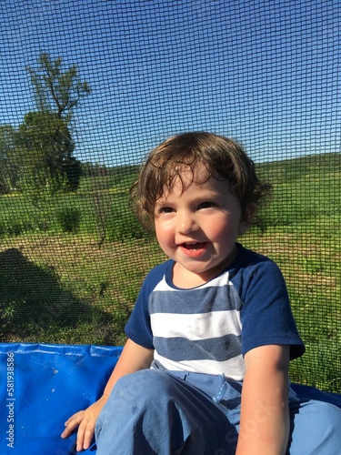 cheerful laughing curly playful little funny boy with beautiful smiling eyes sits on a trampoline