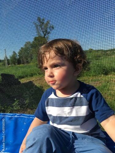 curly cute smiling child sits resting on a trampoline looks with a serious look