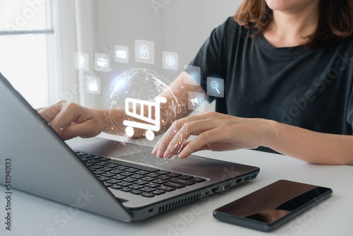 Online shopping and e-commerce concept. Hand of a young businesswoman using a laptop computer and smartphone with a shopping cart icon.