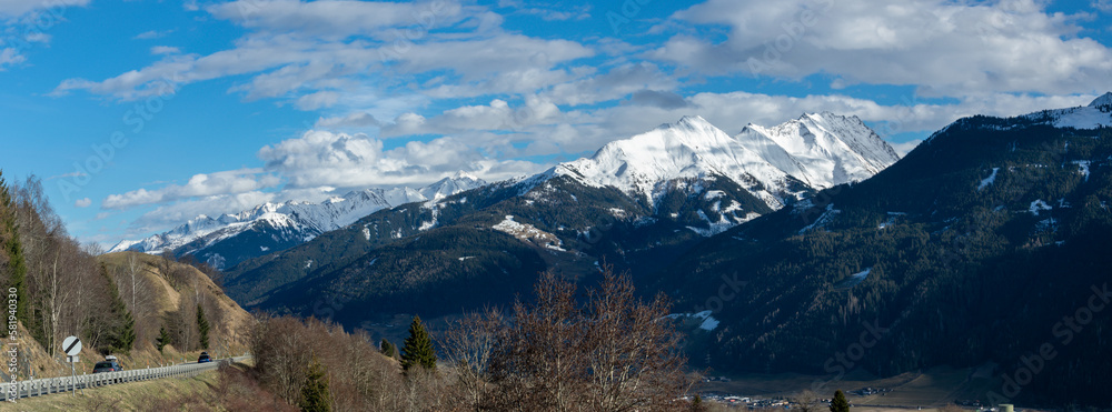 Panorama of Austrian Alps with snowy peaks and deep valley in early spring.