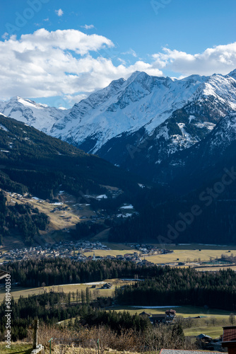 A valley in the Austrian Alps, snowy peaks of rocky mountains and a valley with meadows and a village.