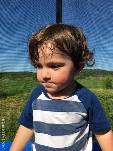 thoughtful cute curly boy walks on a trampoline
