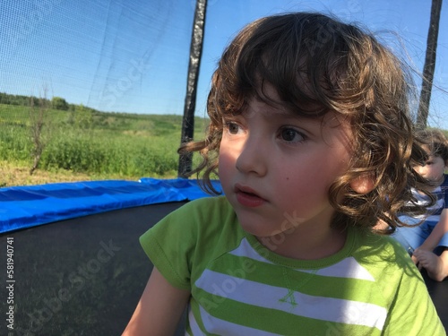 cute curly child surprised boy looks thoughtfully sits on a trampoline