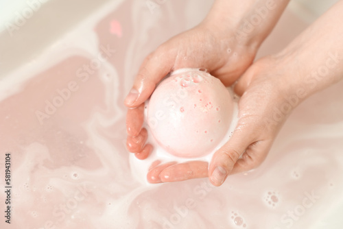 Woman with bath bomb above water, closeup