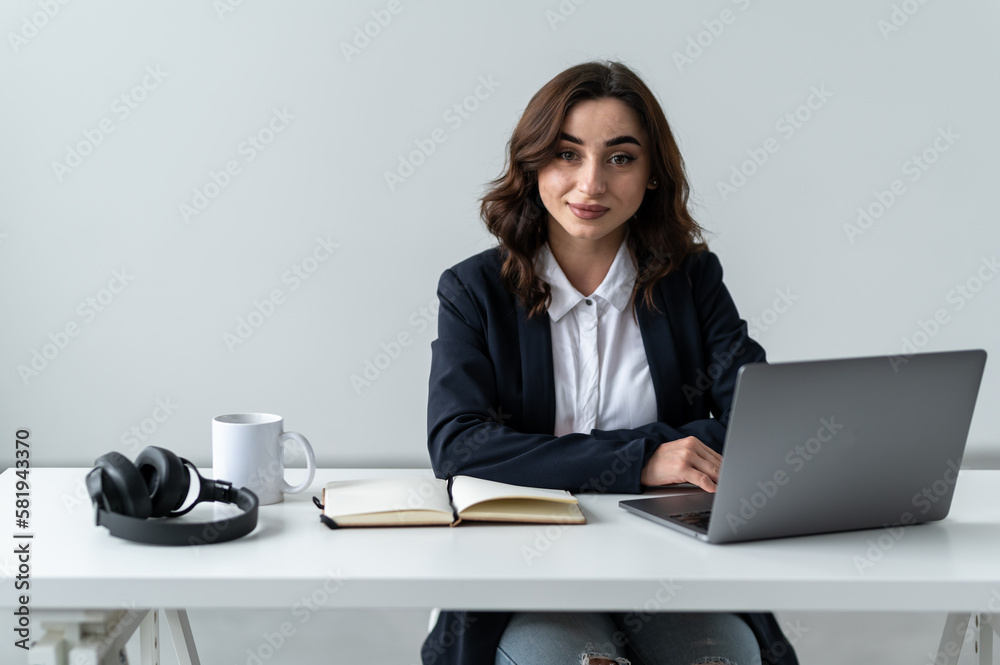An attractive woman is sitting at a workplace. A notebook, headphones and a cup are on the table An attractive woman is sitting at a workplace. A notebook, headphones and a cup are on the table