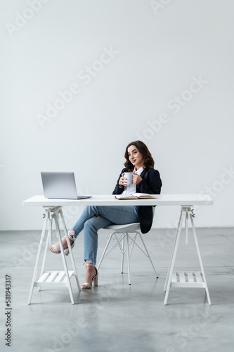 An attractive woman is sitting at the workplace with a cup of coffee and resting after the work done