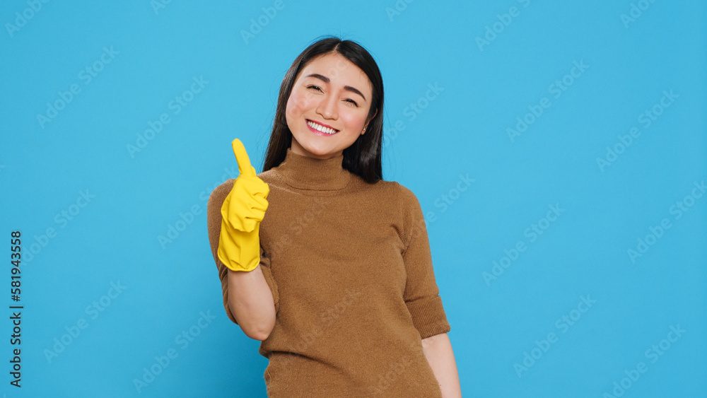 Smiling maid wearing yellow rubber gloves while doing ok gesture after finishing to clean client house, posing in studio. Cheerful housekeeper is responsible for providing cleaning services Smiling maid wearing yellow rubber gloves while doing ok gesture after finishing to clean client house, posing in studio. Cheerful housekeeper is responsible for providing cleaning services