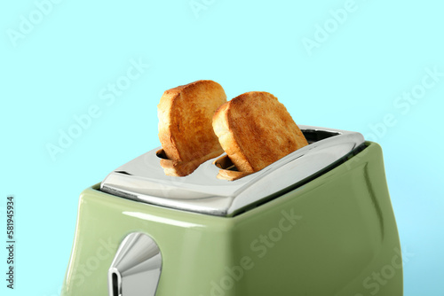 Modern toaster with crispy bread slices on blue background