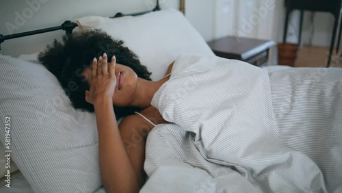 Drowsy model awaking at bed. Curly hairstyle sleepy woman hiding under blanket