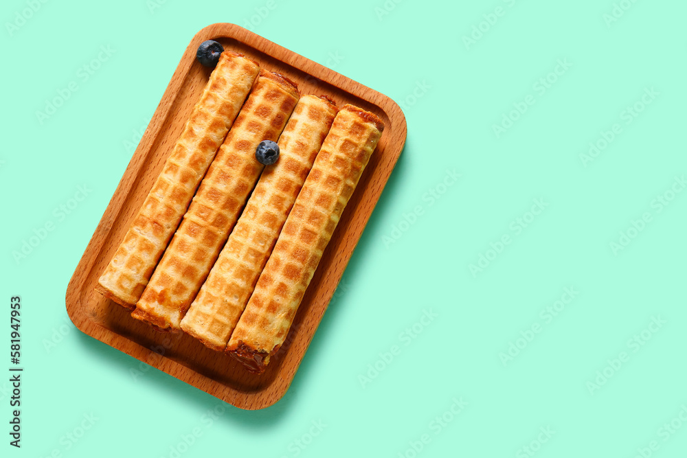 Board of wafer rolls with boiled condensed milk on turquoise background