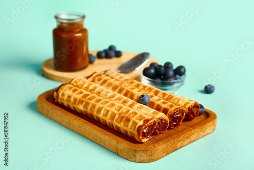 Board of wafer rolls with boiled condensed milk and blueberries on turquoise background