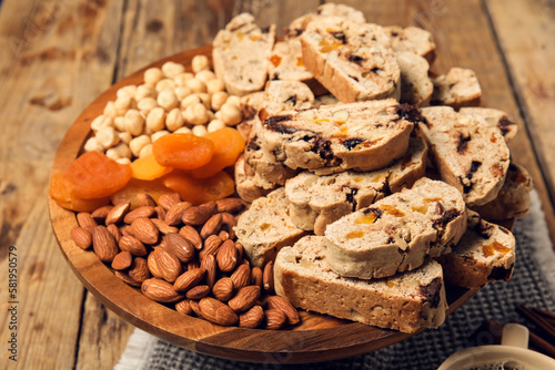 Board with delicious biscotti cookies, dried apricots and nuts on wooden background
