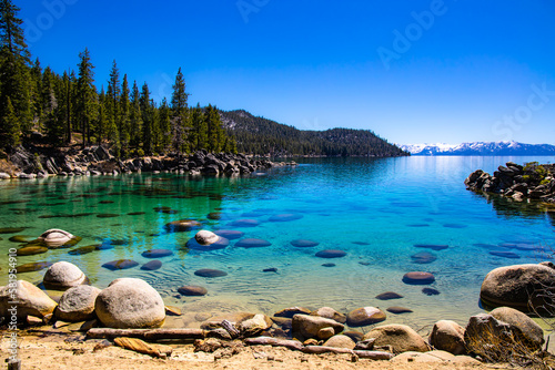 Secret Cove Beach, Lake Tahoe on clear day, crystal clear waters, with snow-covered mountains of the Sierra Nevada in the background