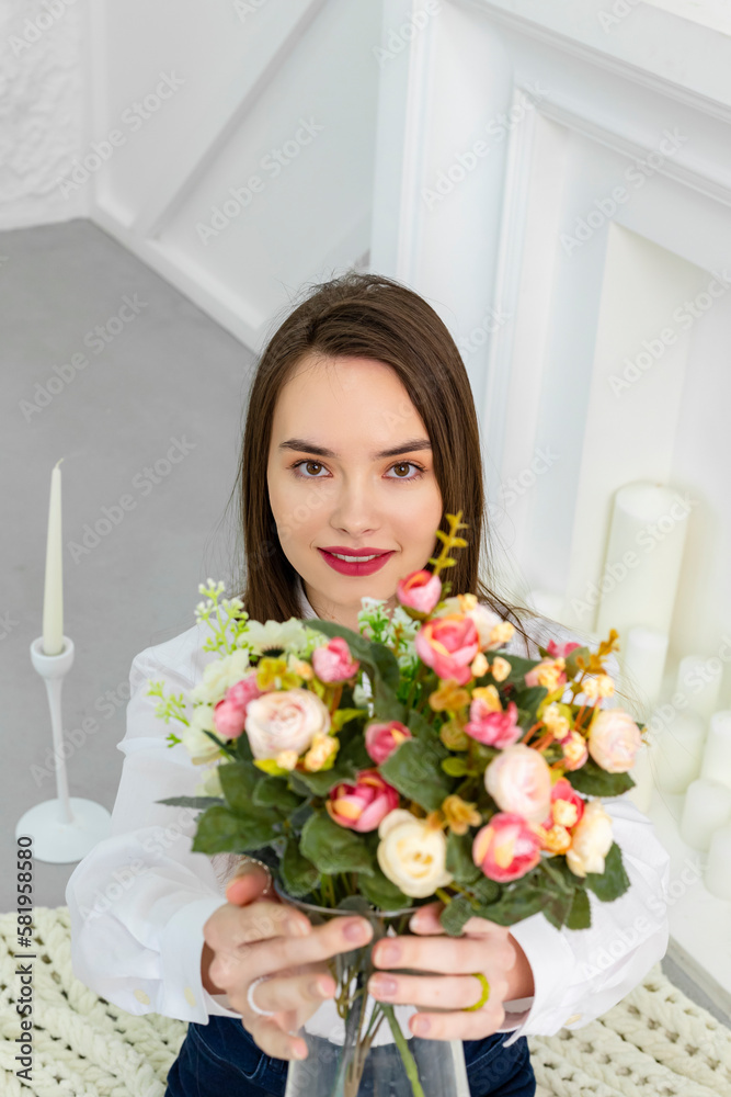 A young young beautiful and cute brown-eyed girl in a white shirt holding a bouquet of flowers towards a camera. Beauty and Freshness concept. A young young beautiful and cute brown-eyed girl in a white shirt holding a bouquet of flowers towards a camera. Beauty and Freshness concept.