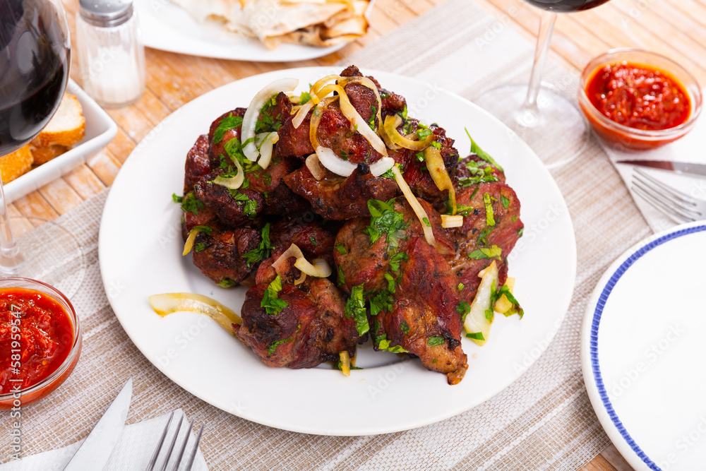 Fototapeta premium Delicious pork shashlik with adzhika sauce and sliced onion rings on a plate in a restaurant