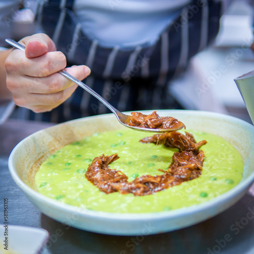 A bowl of chicken pasta and peas with a spoon in it.