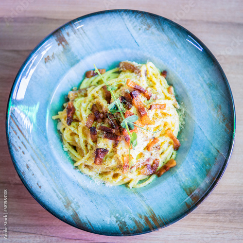 A bowl of spaghetti with bacon and green sauce.