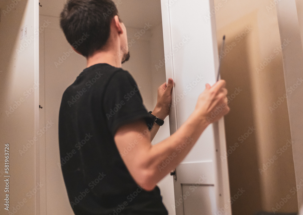 A young man holds the side door of a wardrobe. A young man holds the side door of a wardrobe.