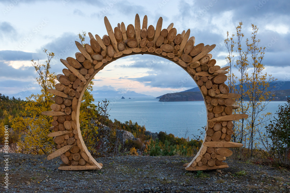 Fototapeta premium Wooden arch at the observation deck. Evening view of the sea. In the distance is a cape and rocks in the sea. Ecological tourism and nature travel. Gertner Bay, Sea of Okhotsk, Magadan region, Russia.